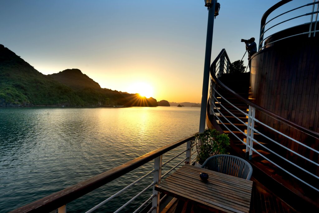 Side view of anonymous male silhouette taking photo on mount and shiny sun on camera from motorboat on lake in evening